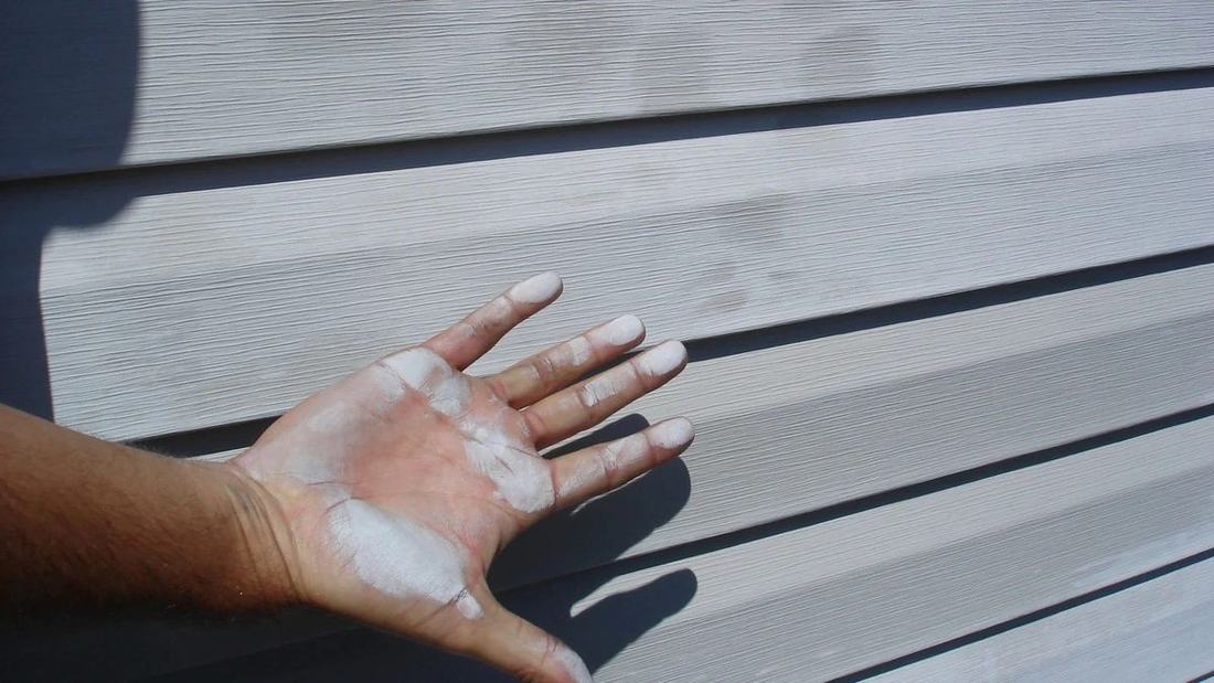 A hand covered in white chalky oxidation after touching faded vinyl siding